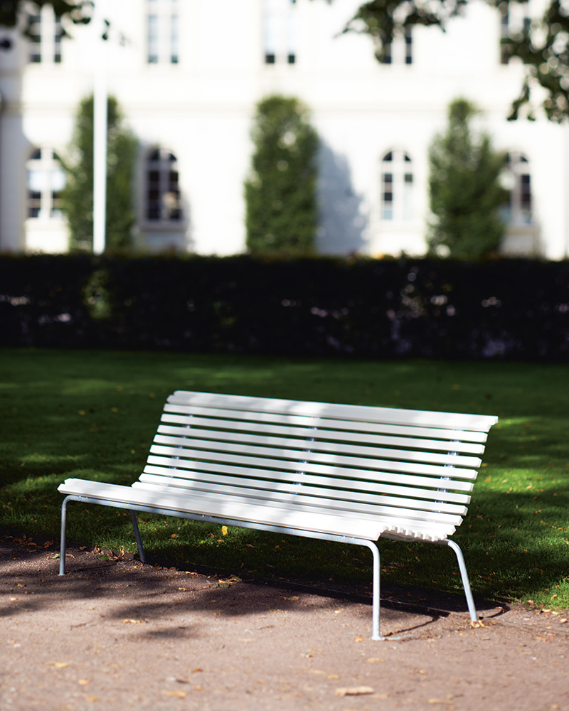 A white Stockholm park bench in a green park.
